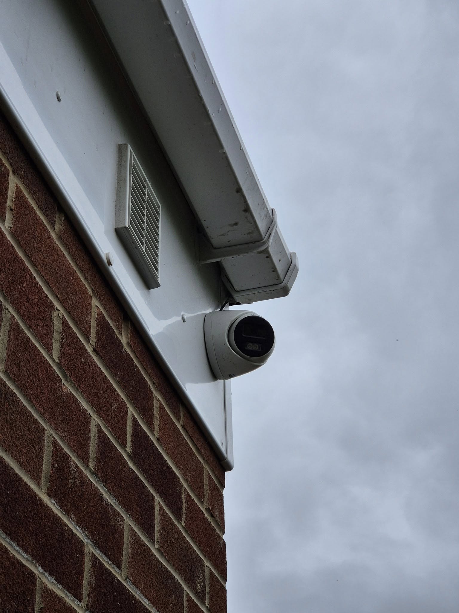 A dome camera mounted under the eaves of a brick house