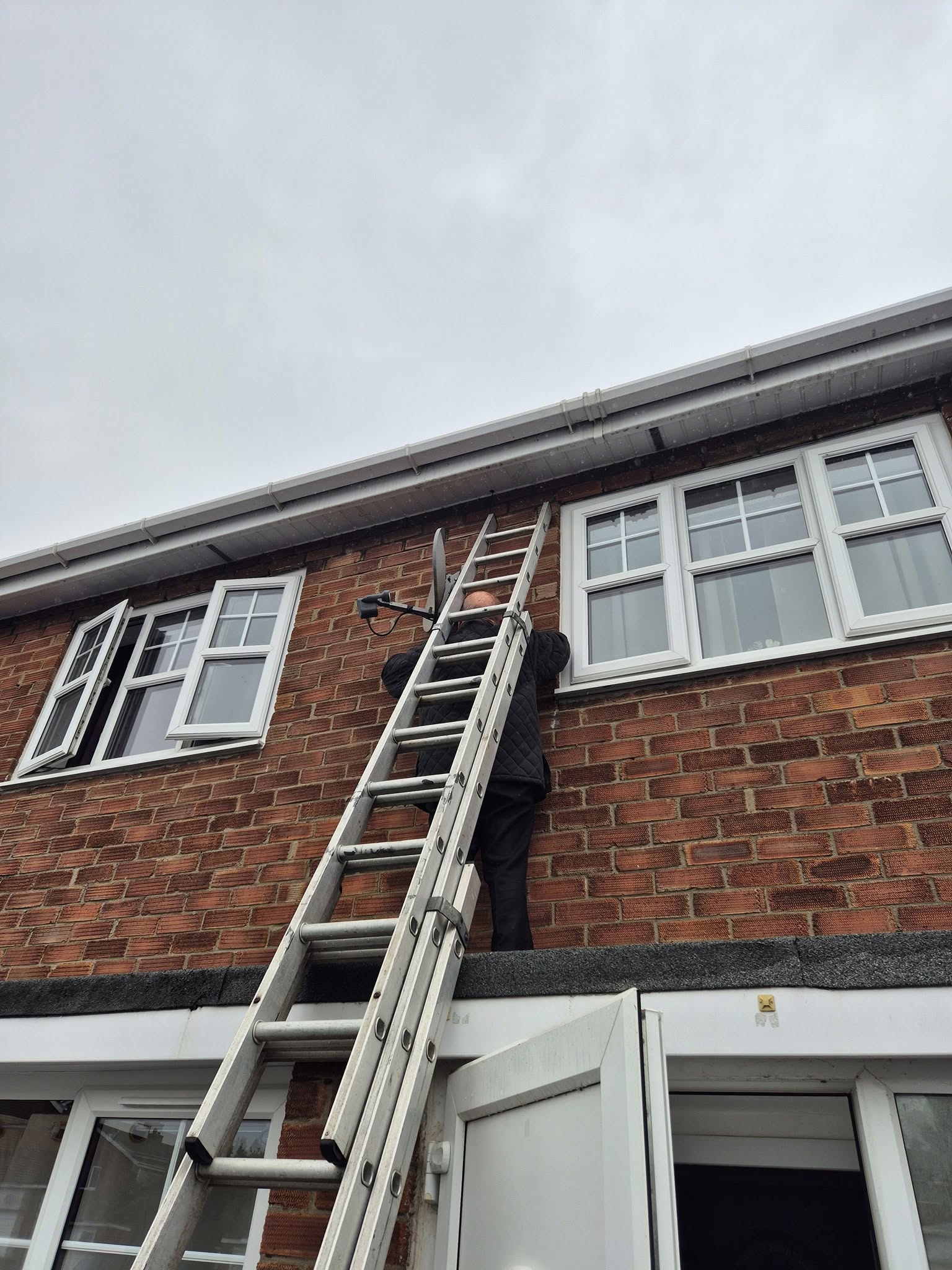 An installer up a ladder fitting a CCTV camera near the roofline