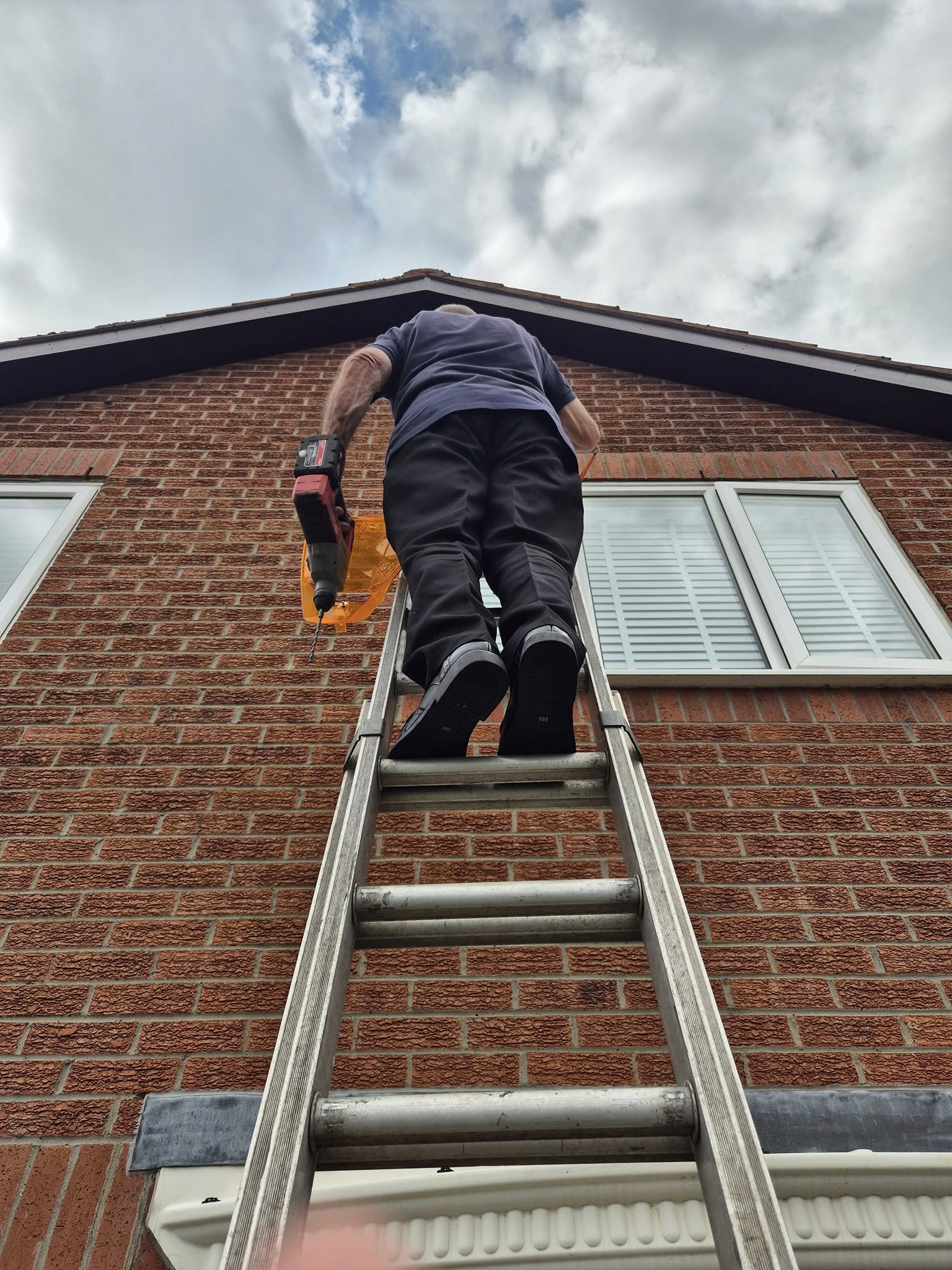 An installer up a ladder drilling into brickwork to route a hidden CCTV cable